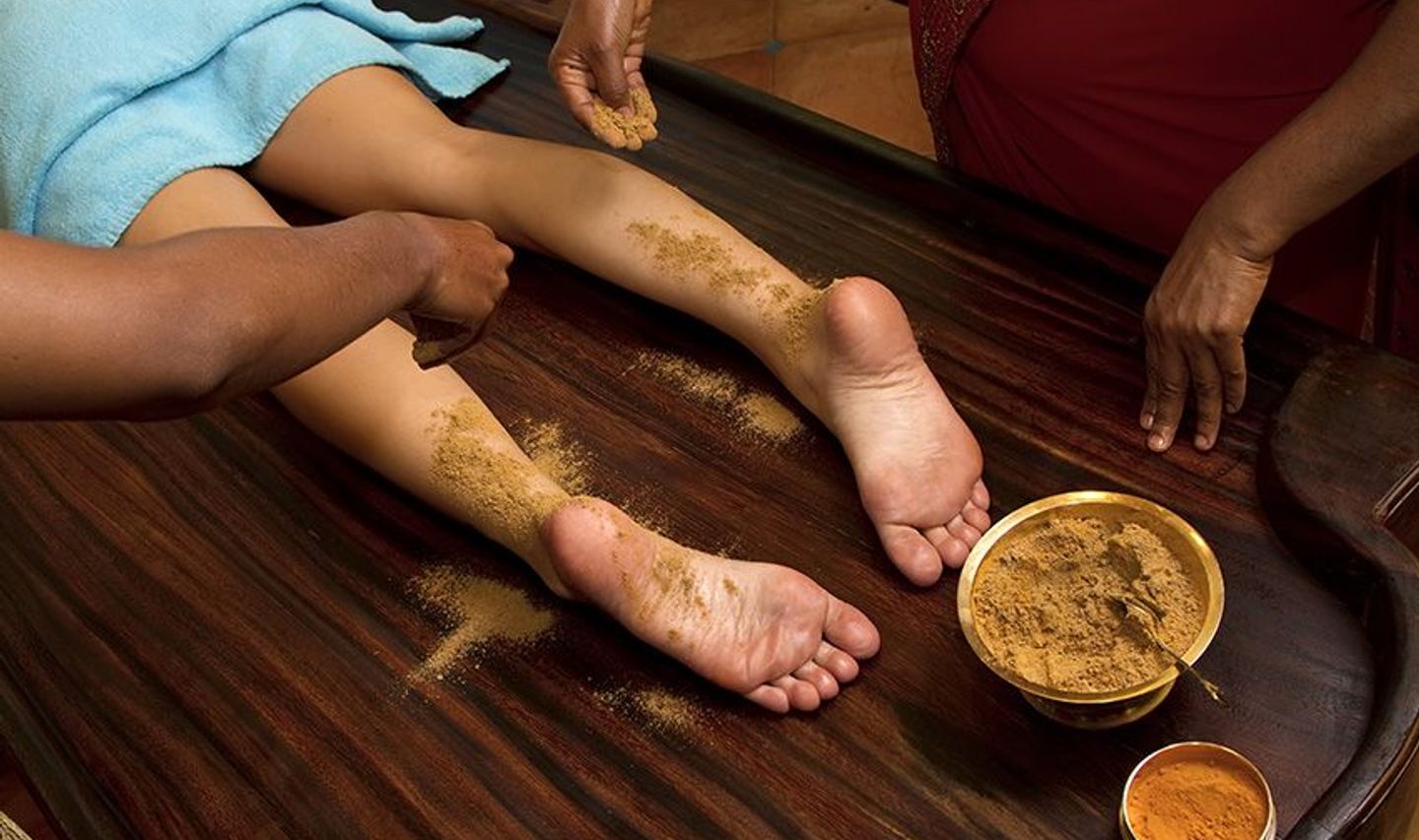 Travel in Asia - Person resting with herbal paste applied to their feet during an Ayurvedic treatment known as Udvartana, with small bowls of natural ingredients nearby