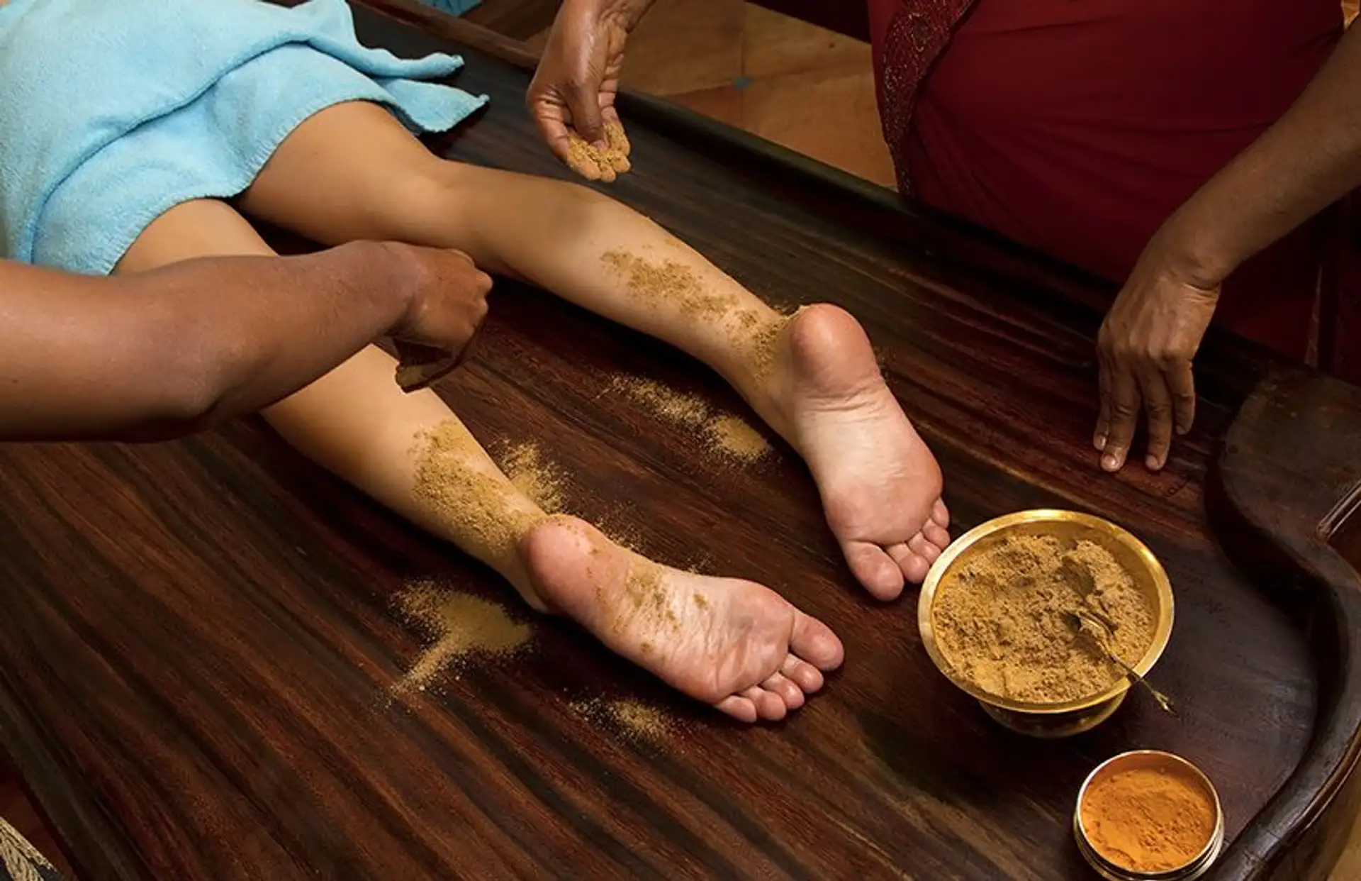 Travel in Asia - Person resting with herbal paste applied to their feet during an Ayurvedic treatment known as Udvartana, with small bowls of natural ingredients nearby
