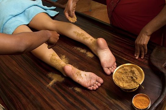 Travel in Asia - Person resting with herbal paste applied to their feet during an Ayurvedic treatment known as Udvartana, with small bowls of natural ingredients nearby