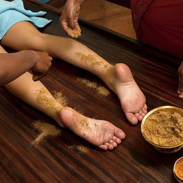 Travel in Asia - Person resting with herbal paste applied to their feet during an Ayurvedic treatment known as Udvartana, with small bowls of natural ingredients nearby