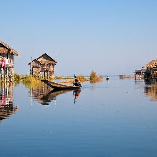 Travel in Asia - A person on boat on a calm Inle Lake with stilt houses in the background
