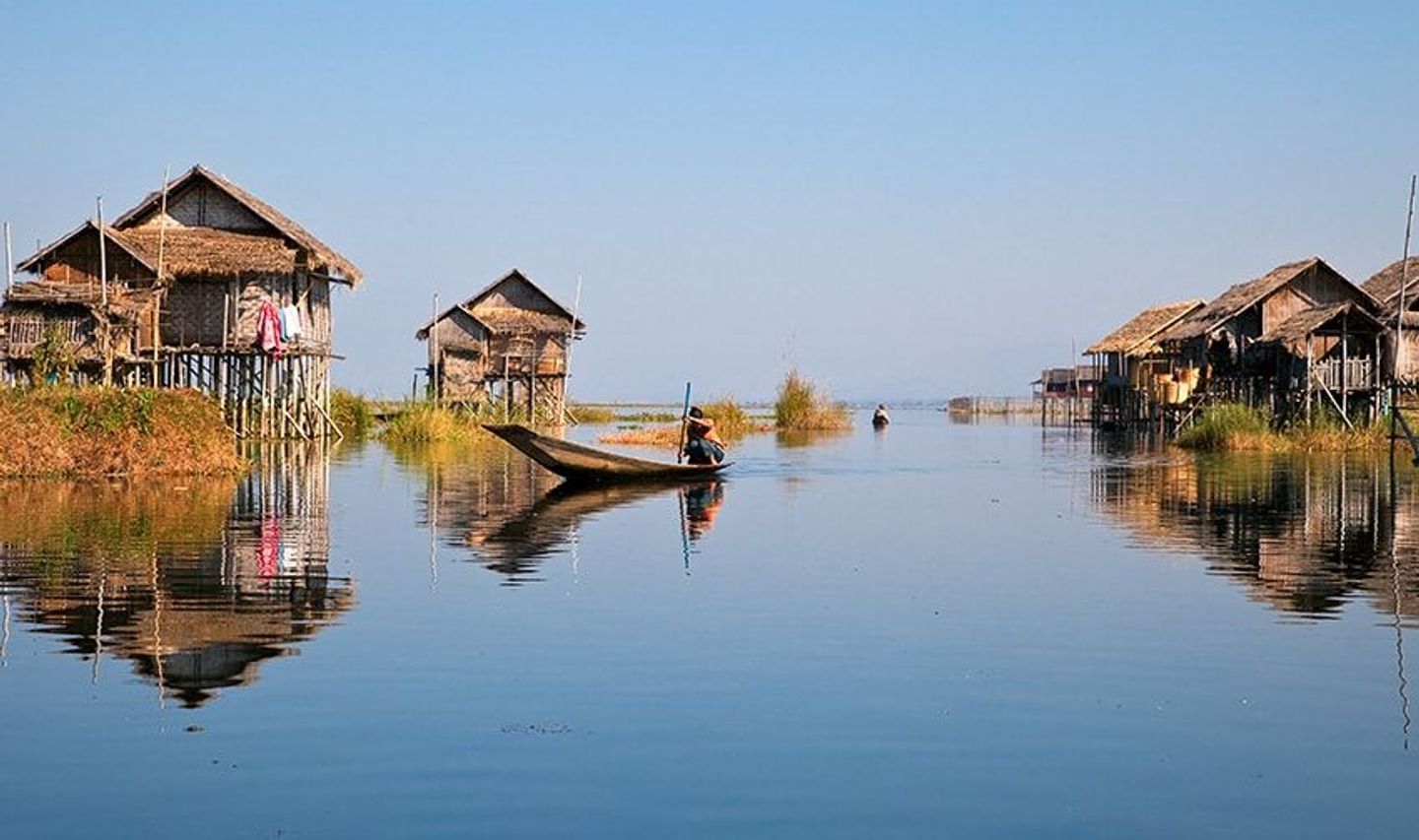 Travel in Asia - A person on boat on a calm Inle Lake with stilt houses in the background