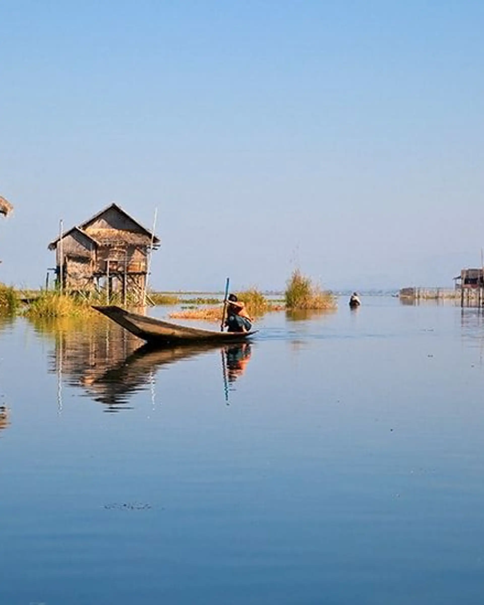 Travel in Asia - A person on boat on a calm Inle Lake with stilt houses in the background