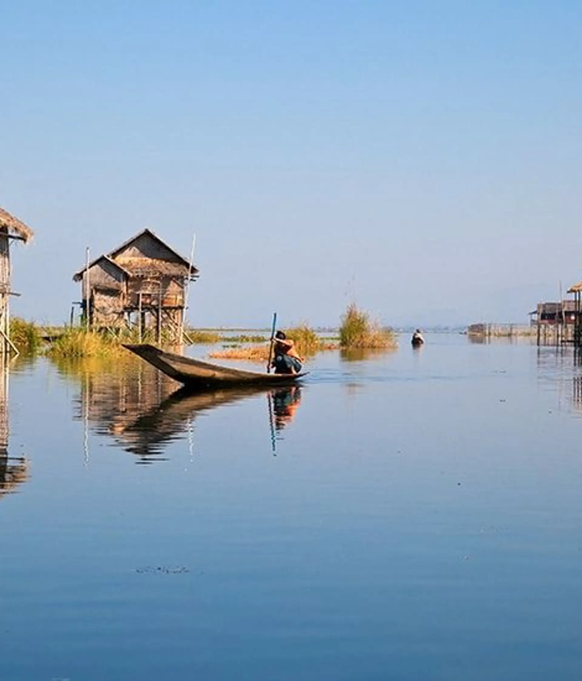 Travel in Asia - A person on boat on a calm Inle Lake with stilt houses in the background
