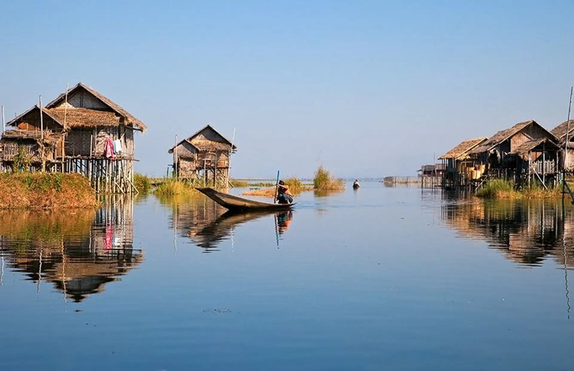 Travel in Asia - A person on boat on a calm Inle Lake with stilt houses in the background