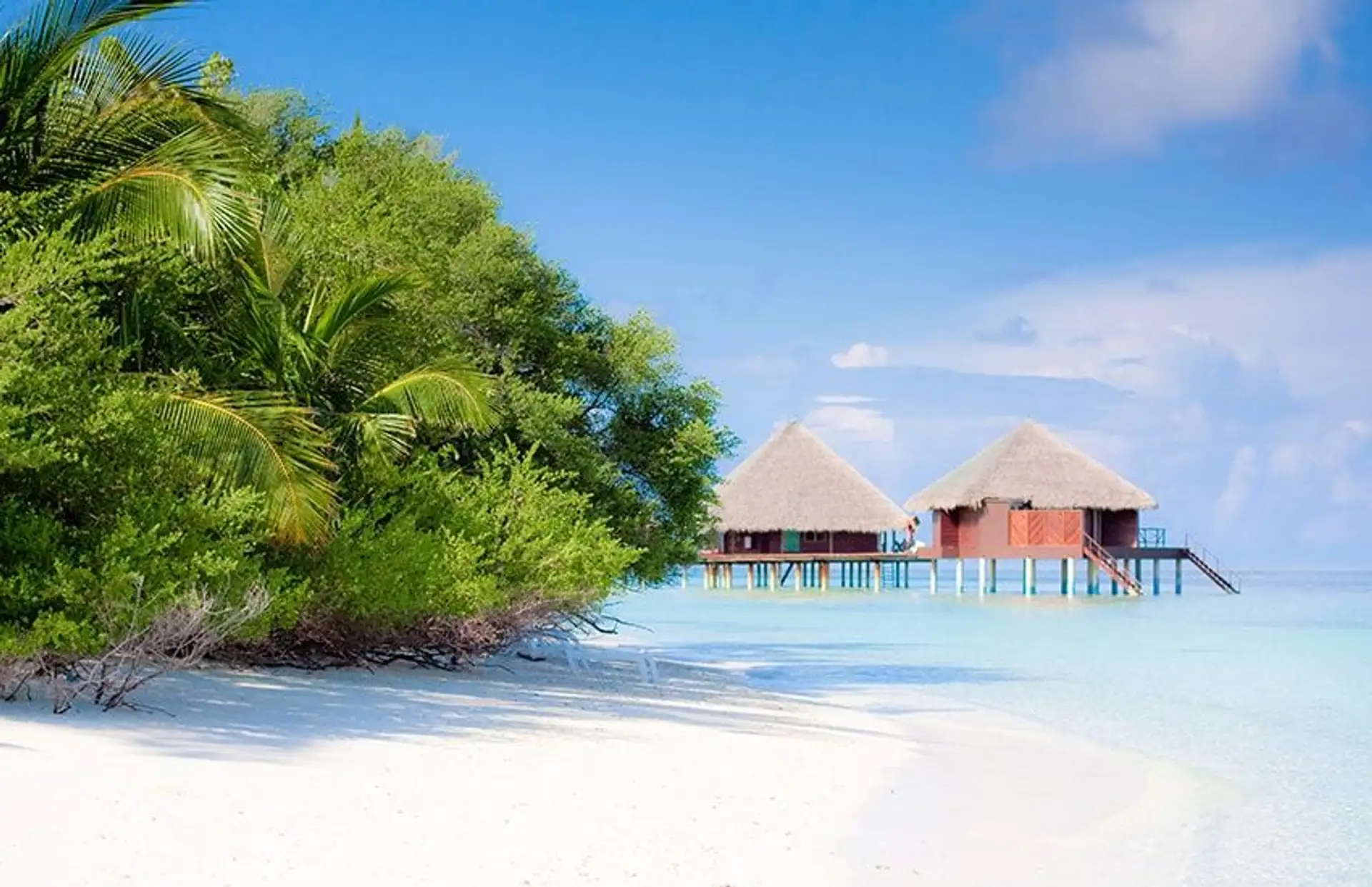 Travel in Asia - Two overwater villas on a white-sand beach on a clear, sunny day in the Maldives