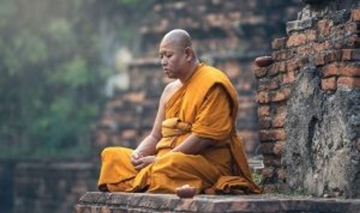 Travel in Asia - A Buddhist monk sitting cross-legged on a temple grounds in meditation in Myanmar