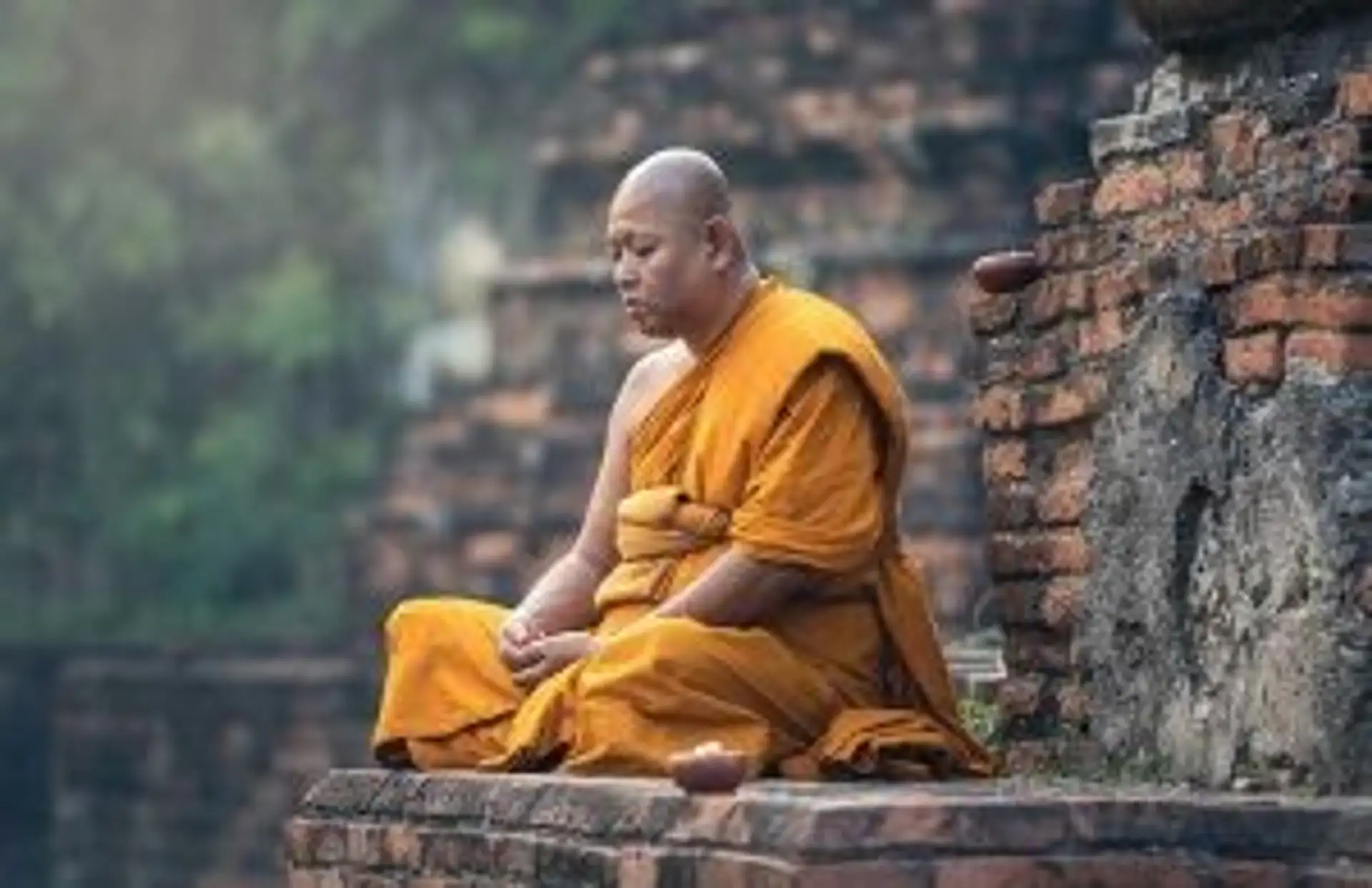 Travel in Asia - A Buddhist monk sitting cross-legged on a temple grounds in meditation in Myanmar