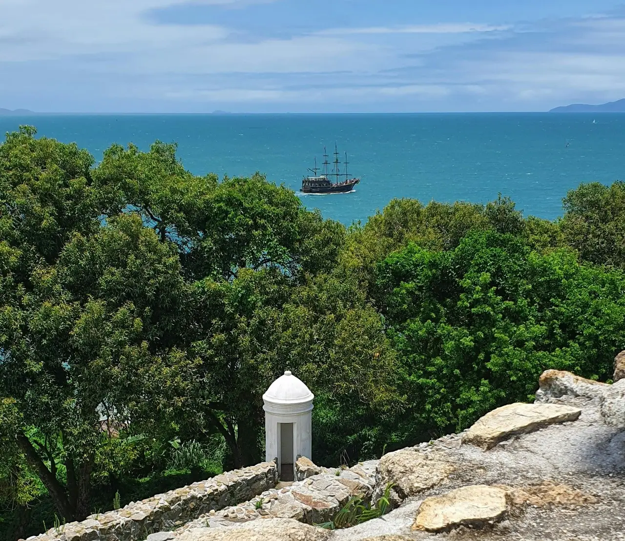 Voyage au Brésil – Vue panoramique sur l'océan Atlantique et un voilier traditionnel au loin depuis les remparts en pierre du fort historique de Praia do Forte.