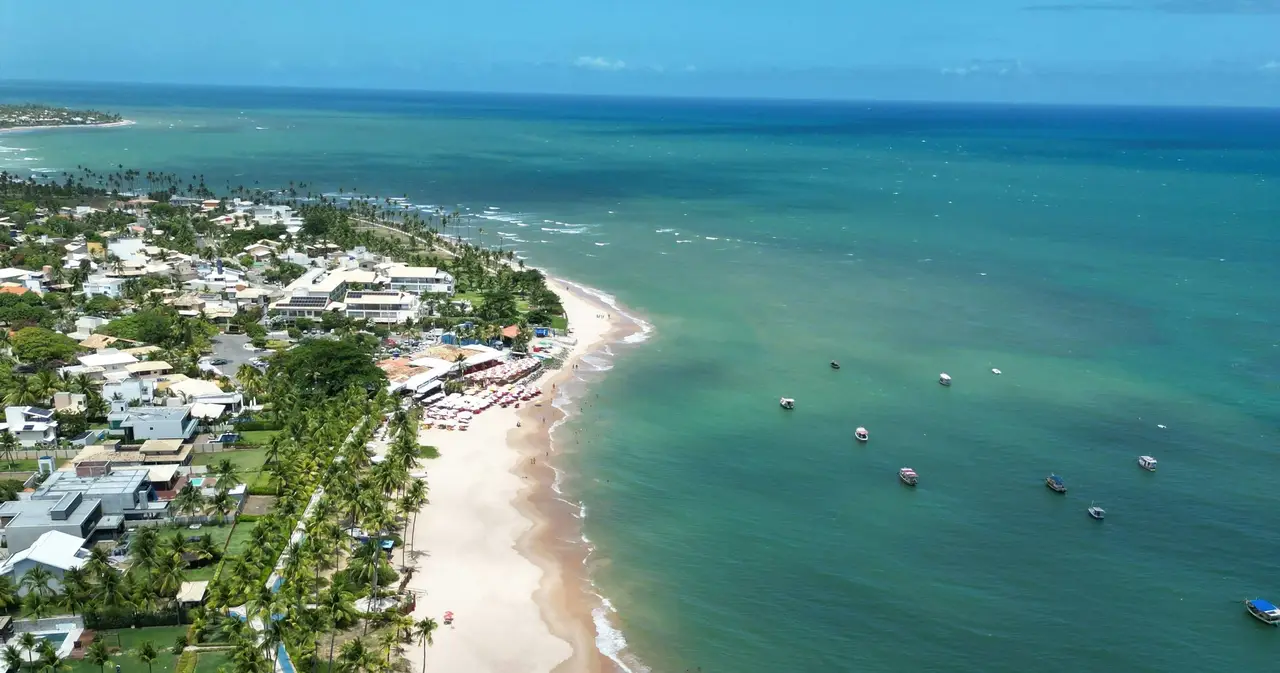 Voyage au Brésil – Vue aérienne panoramique du village littoral de Praia do Forte bordé par une plage de sable fin et des eaux tropicales turquoise à Bahia.