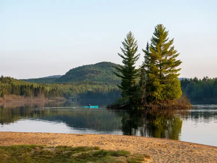 Îlot boisé de conifères sur un lac calme avec collines verdoyantes à l'horizon dans la région de la Mauricie