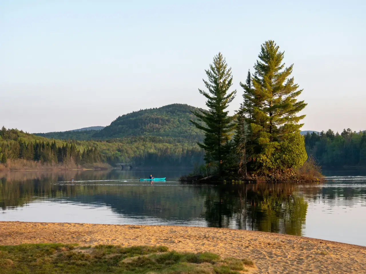 Îlot boisé de conifères sur un lac calme avec collines verdoyantes à l'horizon dans la région de la Mauricie