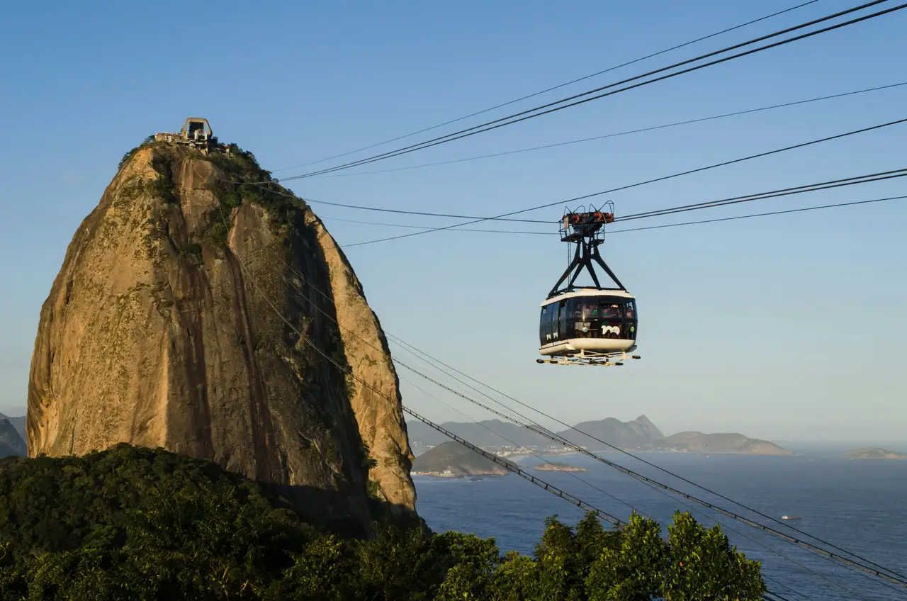 Voyage au Brésil – La cabine du téléphérique suspendue sur ses câbles s'approchant du sommet rocheux du Pain de Sucre à Rio de Janeiro.