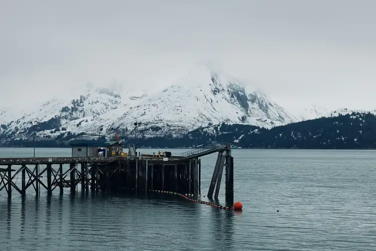 Ponton en bois sur les eaux calmes d'un fjord face à une imposante montagne couverte de neige sous un ciel brumeux à Valdez en Alaska
