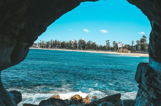 Ouverture d'une grotte rocheuse révélant la plage de Manly et l'océan