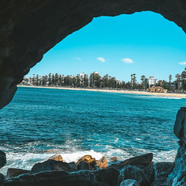 Ouverture d'une grotte rocheuse révélant la plage de Manly et l'océan
