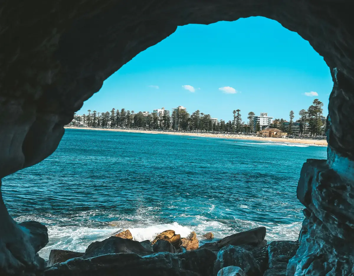 Ouverture d'une grotte rocheuse révélant la plage de Manly et l'océan