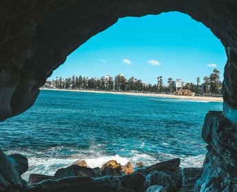 Ouverture d'une grotte rocheuse révélant la plage de Manly et l'océan