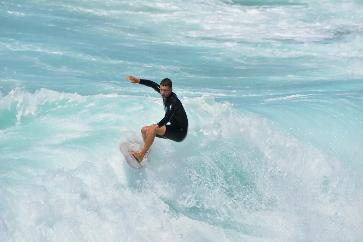 Jeune surfeur en combinaison glissant sur une vague d'eau turquoise à Manly Beach