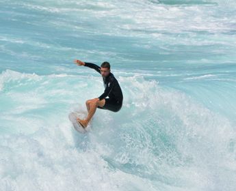 Jeune surfeur en combinaison glissant sur une vague d'eau turquoise à Manly Beach