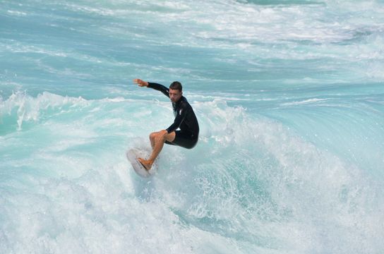 Jeune surfeur en combinaison glissant sur une vague d'eau turquoise à Manly Beach