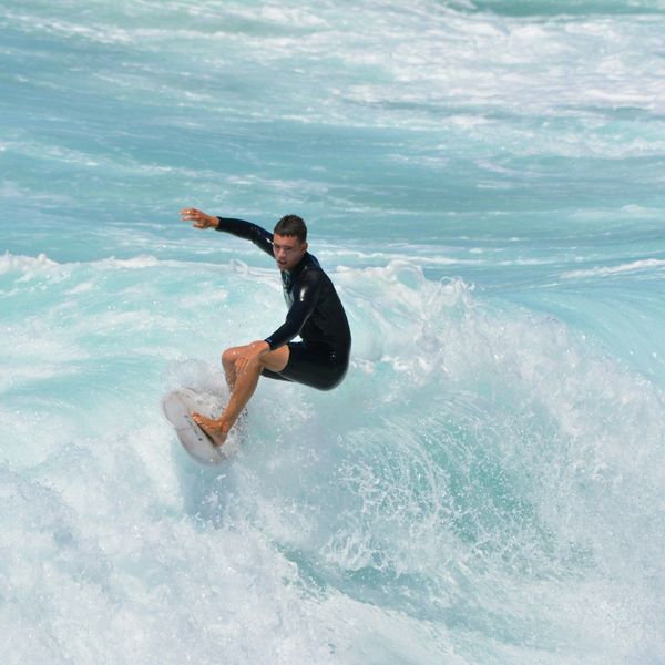 Jeune surfeur en combinaison glissant sur une vague d'eau turquoise à Manly Beach
