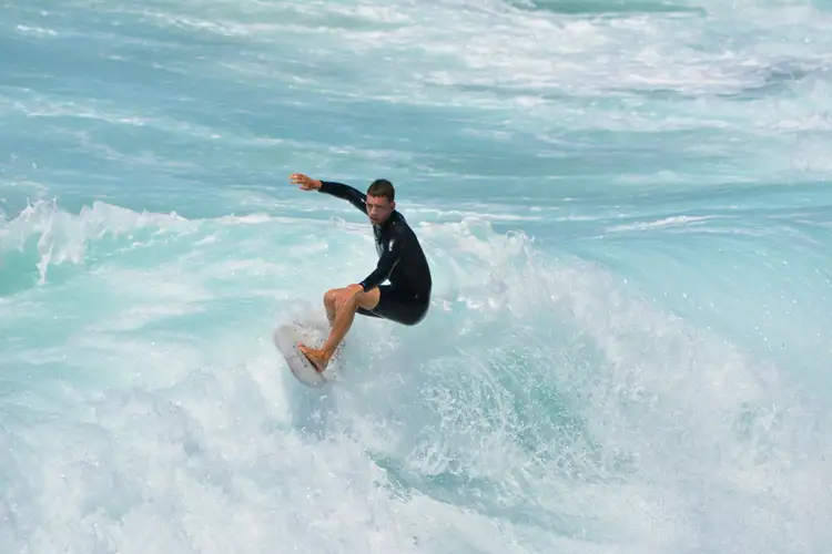 Jeune surfeur en combinaison glissant sur une vague d'eau turquoise à Manly Beach