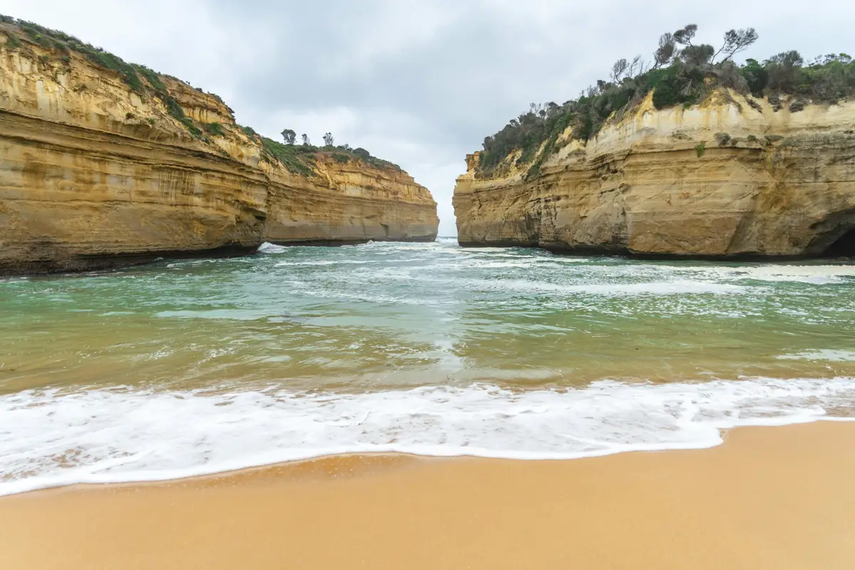 Vagues de l'océan s'engouffrant entre les falaises dorées de Loch Ard Gorge sur la Great Ocean Road
