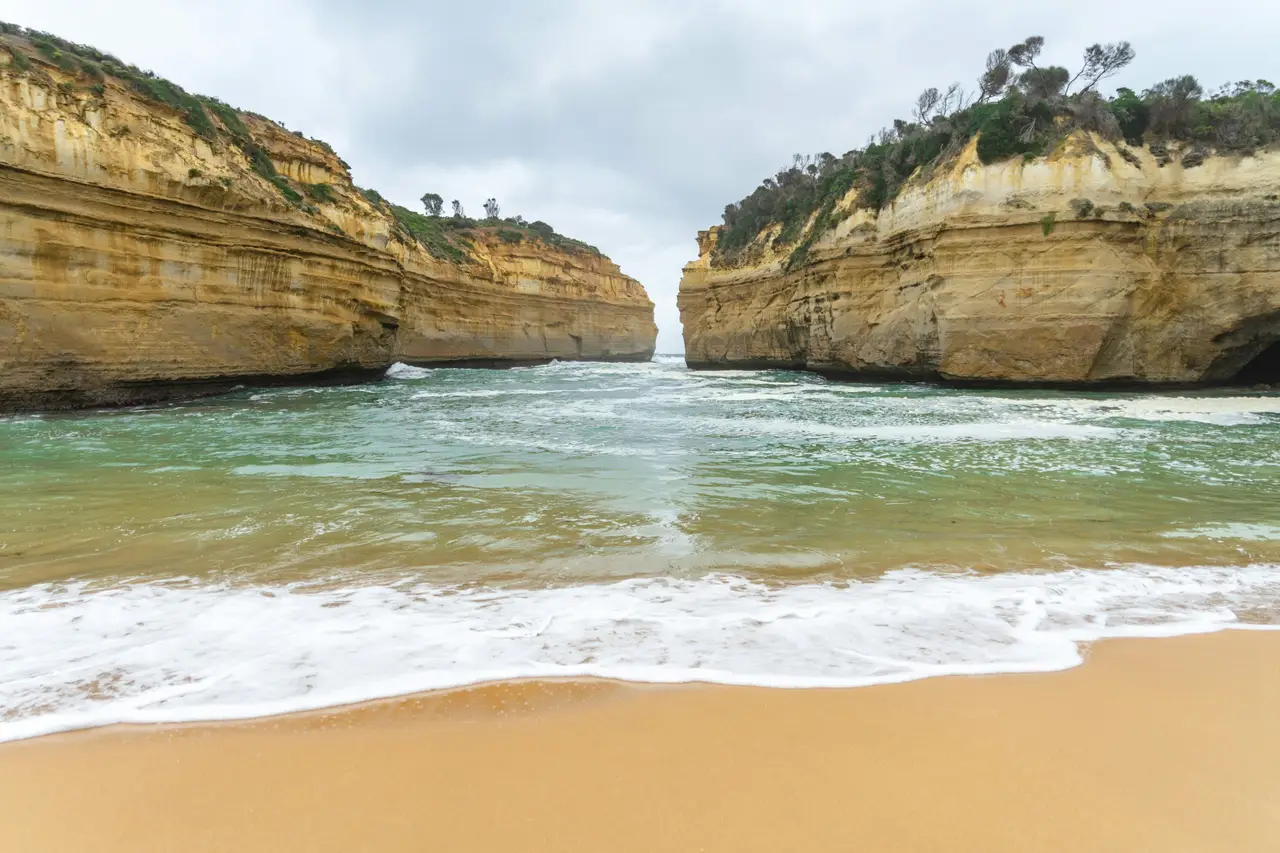 Vagues de l'océan s'engouffrant entre les falaises dorées de Loch Ard Gorge sur la Great Ocean Road