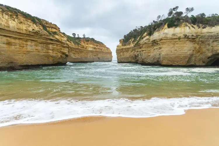 Vagues de l'océan s'engouffrant entre les falaises dorées de Loch Ard Gorge sur la Great Ocean Road