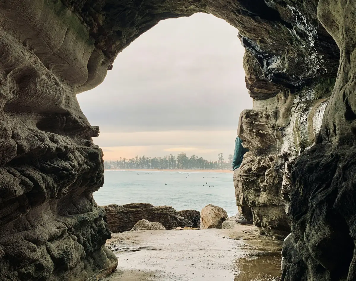 Grotte rocheuse s'ouvrant sur les eaux claires et les surfeurs au large de Manly Beach