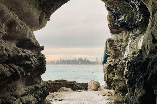Grotte rocheuse s'ouvrant sur les eaux claires et les surfeurs au large de Manly Beach
