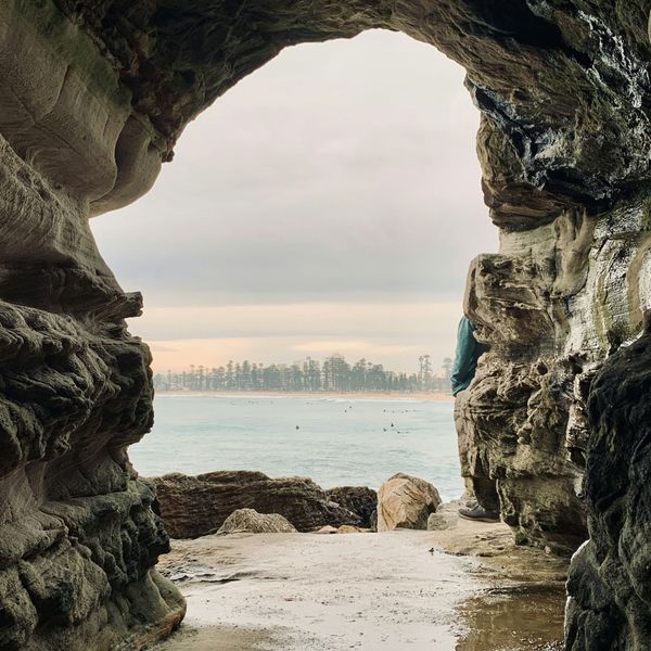 Grotte rocheuse s'ouvrant sur les eaux claires et les surfeurs au large de Manly Beach