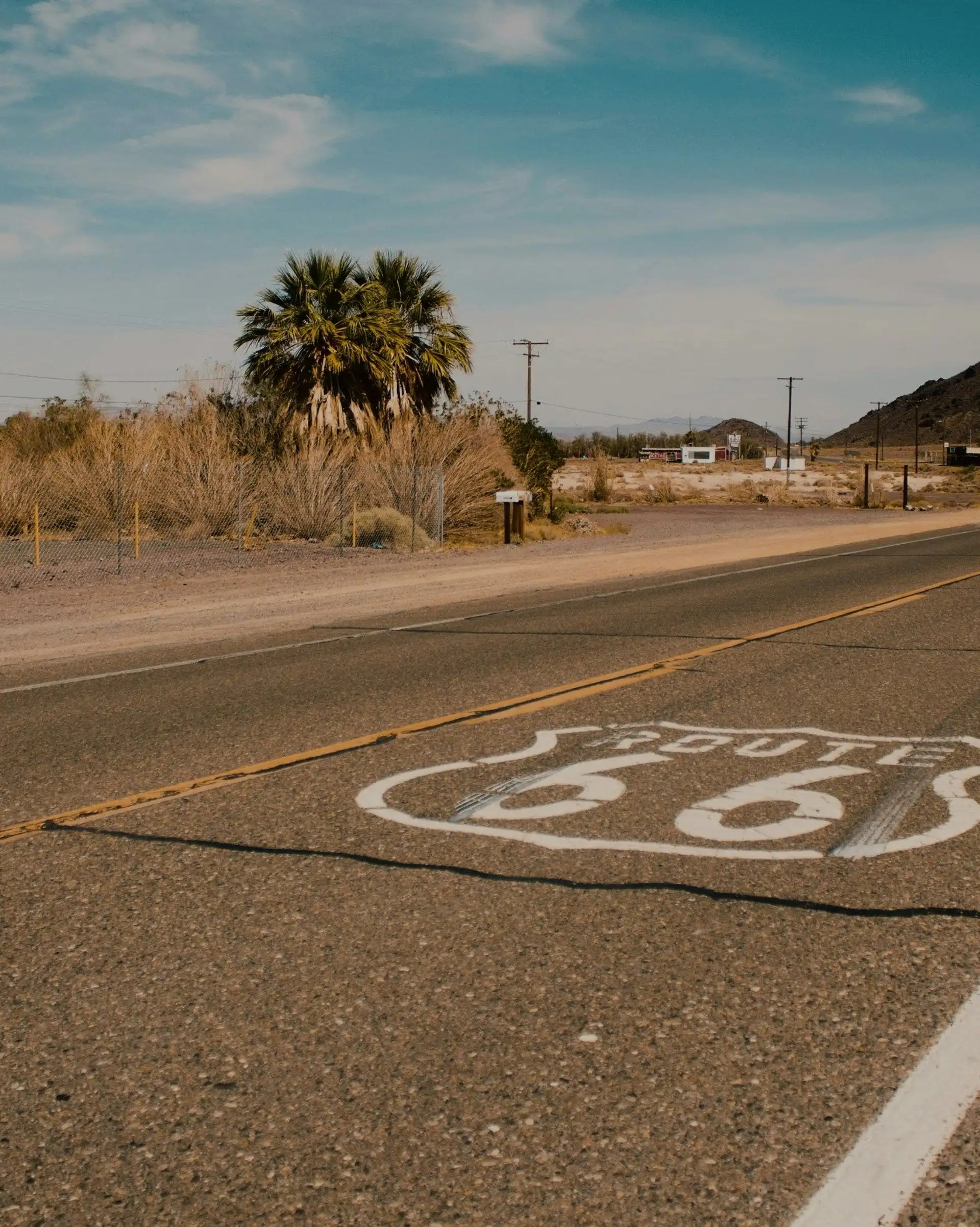 Logo emblématique de la Route 66 peint sur l'asphalte d'une route traversant un paysage désertique et montagneux
