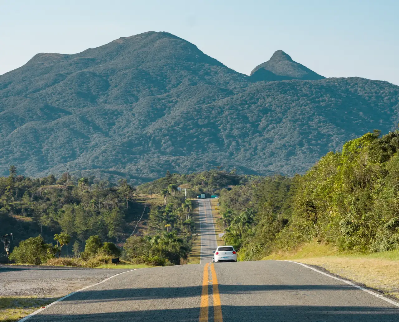 Voyage au Brésil – Longue route asphaltée rectiligne traversant une nature verdoyante en direction de montagnes rocheuses lors d'un road trip vers Bahia.