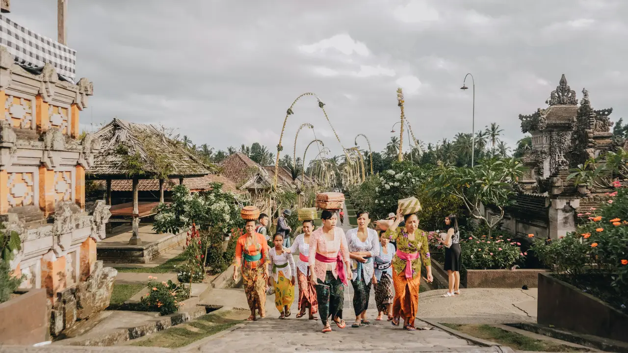 Allée principale pavée du village traditionnel de Penglipuran bordée de maisons balinaises typiques aux portes sculptées et de décorations en bambou sous un ciel nuageux.