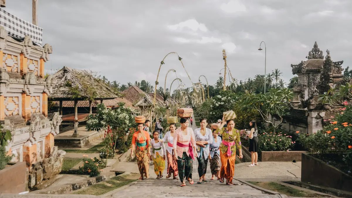 Allée principale pavée du village traditionnel de Penglipuran bordée de maisons balinaises typiques aux portes sculptées et de décorations en bambou sous un ciel nuageux.