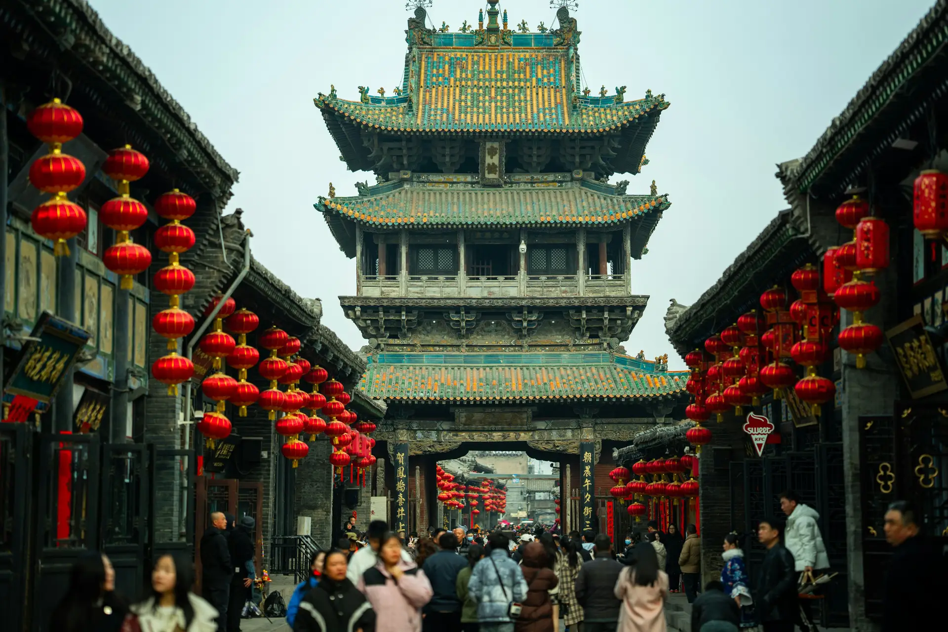 Une imposante tour traditionnelle chinoise en bois aux toits superposés entourée de ruelles décorées de nombreuses lanternes rouges suspendues à Pingyao.