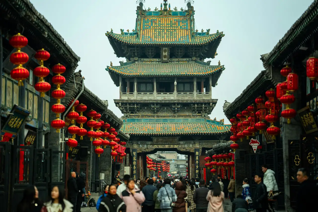 Une imposante tour traditionnelle chinoise en bois aux toits superposés entourée de ruelles décorées de nombreuses lanternes rouges suspendues à Pingyao.
