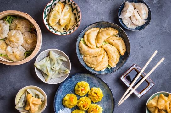 Assortiment de dim sum traditionnels chinois incluant des raviolis vapeur et des siu mai servis dans des bols sur une table.