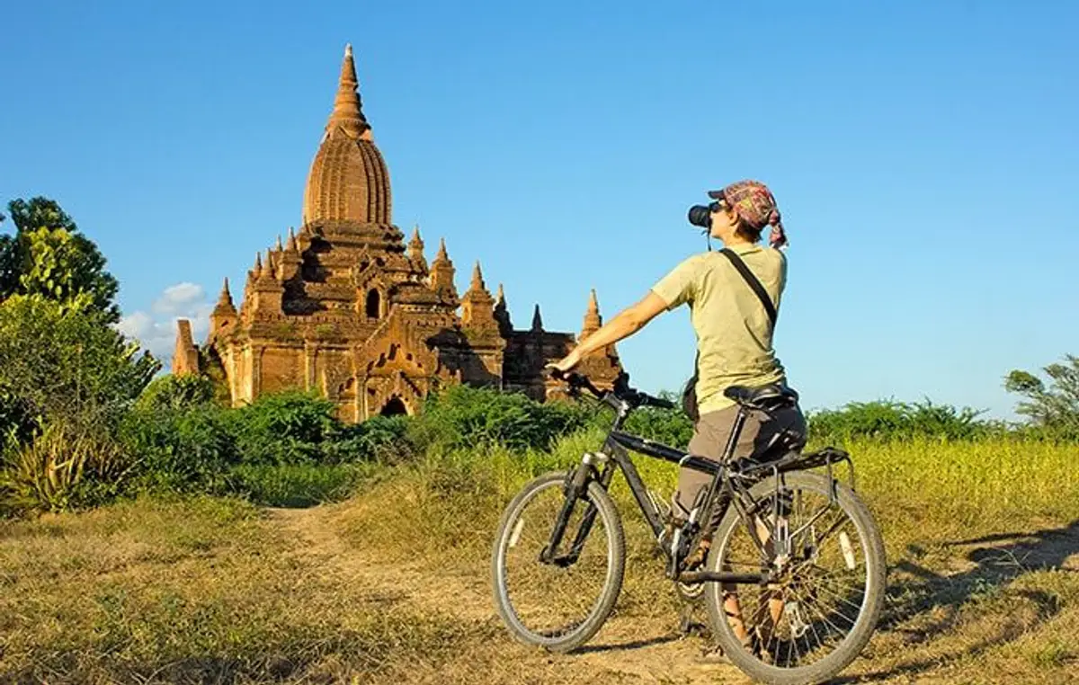 Voyageur à vélo admirant un temple bouddhiste au cœur du site archéologique de Bagan.