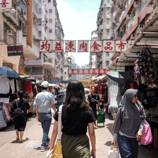 Vue d'une rue animée du marché de Mong Kok à Hong Kong avec des passants, des étals extérieurs et des enseignes chinoises traditionnelles suspendues.