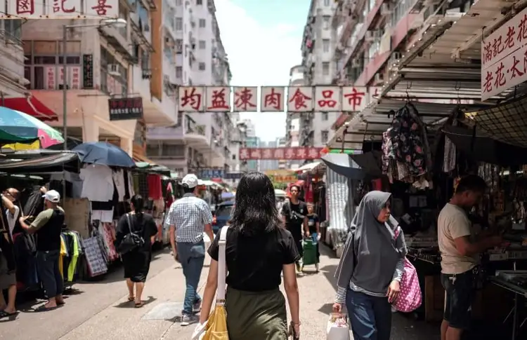 Vue d'une rue animée du marché de Mong Kok à Hong Kong avec des passants, des étals extérieurs et des enseignes chinoises traditionnelles suspendues.