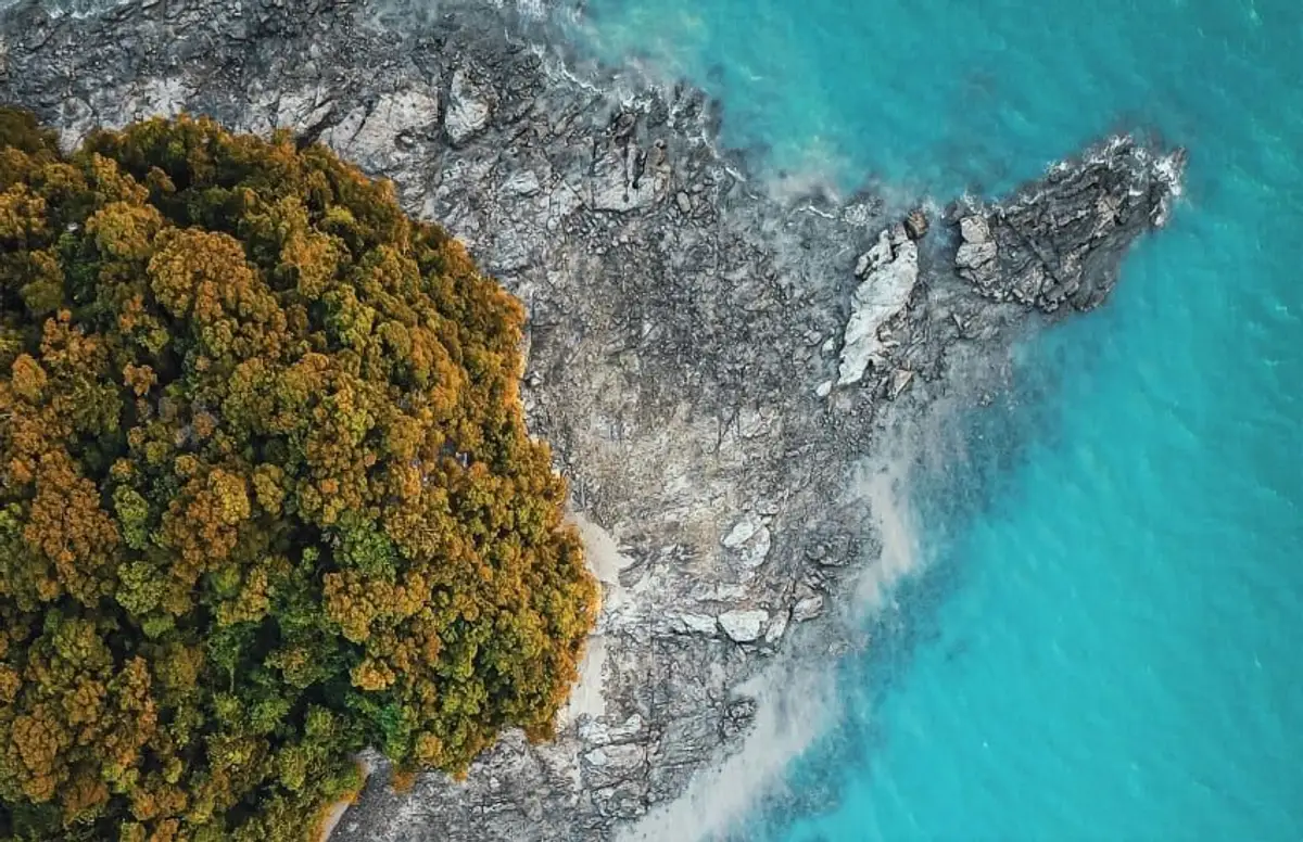 Vue aérienne en plongée d'un cap rocheux et sauvage bordé par une forêt tropicale dense et des eaux côtières turquoise translucides à l'île de Langkawi en Malaisie.