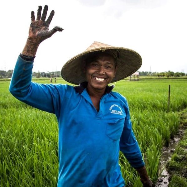 Une femme sourit en tenant une noix de coco fraîche à la main, assise face à l'océan Indien turquoise et au ciel nuageux sur la plage de Jimbaran à Bali.