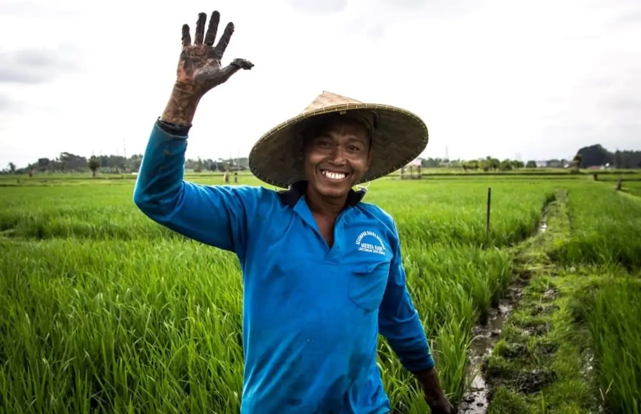 Voyage à Bali – Habitante souriante saluant de la main au cœur de la campagne balinaise pour un au revoir chaleureux.