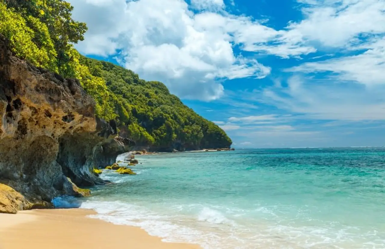 Voyage à Bali – Plage de sable blanc bordée de falaises verdoyantes et eau turquoise sur la presqu'île de Bukit à Jimbaran.