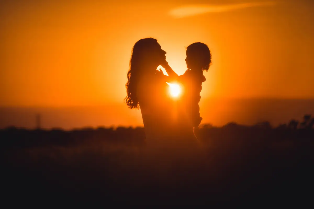 Voyage en Asie : silhouette d’une maman portant son enfant dans un coucher de soleil, moment de tendresse et d’émerveillement.