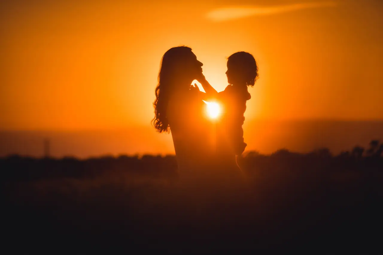 Silhouette d'une mère et de son enfant se tenant tendrement face à face au coucher du soleil, baignés par une lumière dorée et chaleureuse à Sanur.